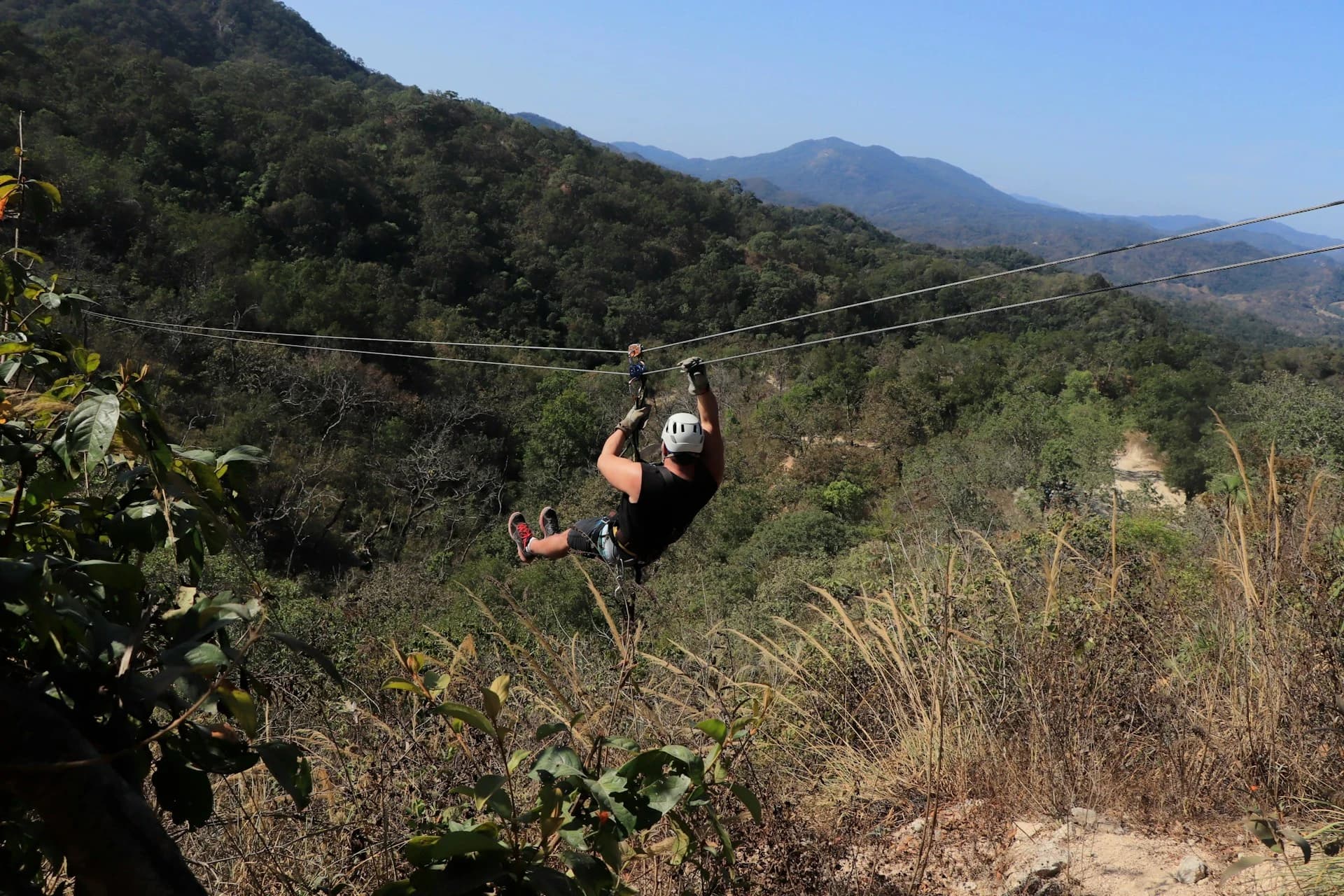 Zipliner in a harness crossing a carbon fiber cable high above green tropical forest near Punta Cana